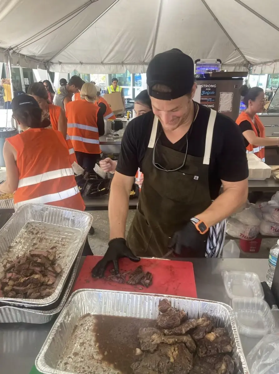 Chef Paul carving beef under the relief tent with volunteers in safety vests