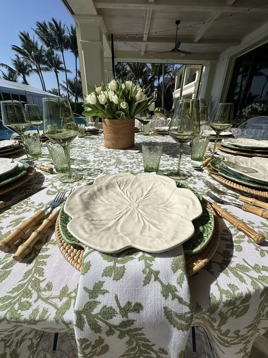 Outdoor table styled with green botanical linens, cabbage-leaf plates, rattan chargers and white tulips