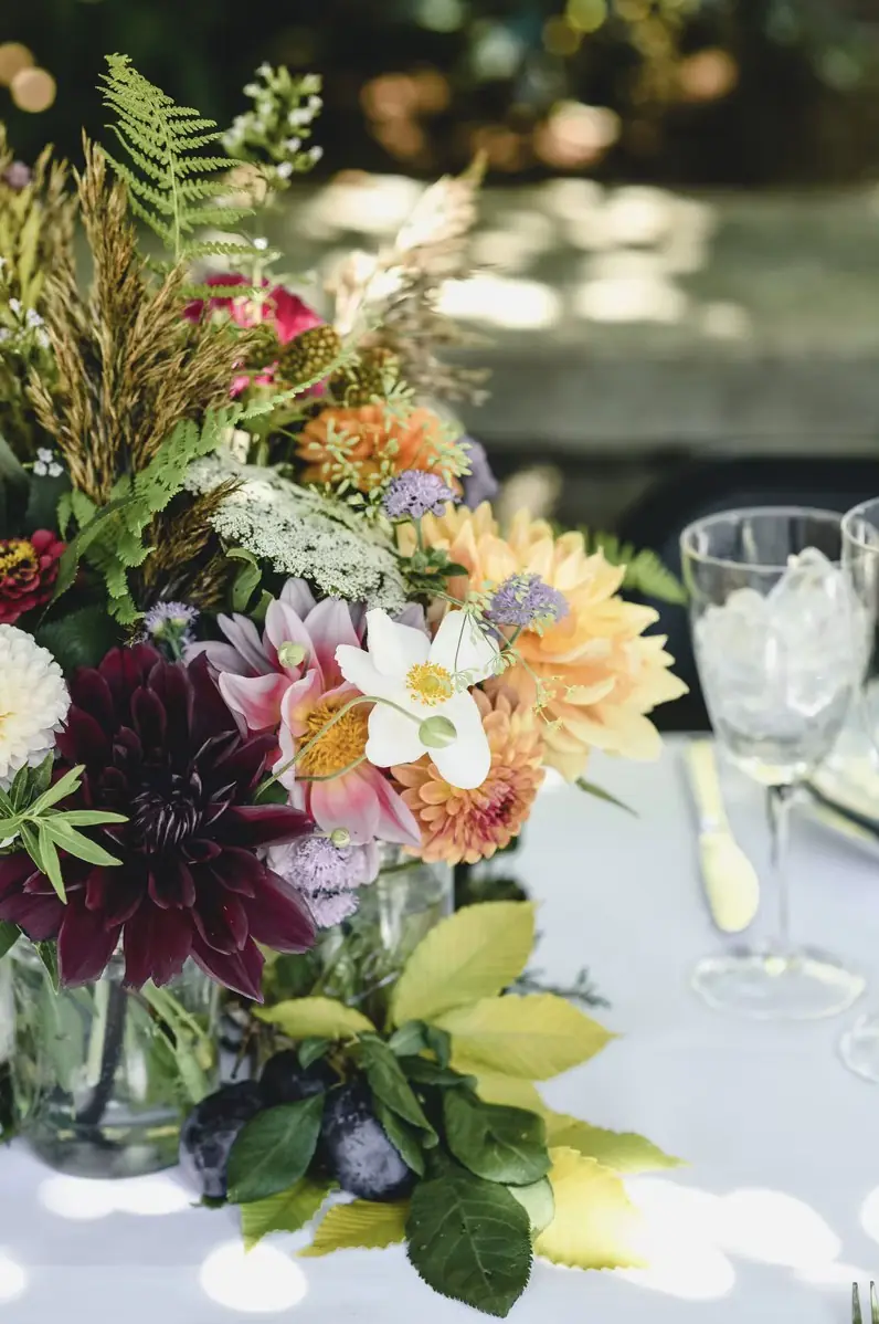 Wedding centerpiece of dahlias, anemones and ferns on a white table set for a celebration