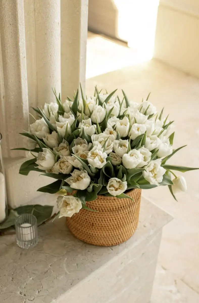 White tulips in a woven rattan basket beside a candle, styled by Silver Spoon Events